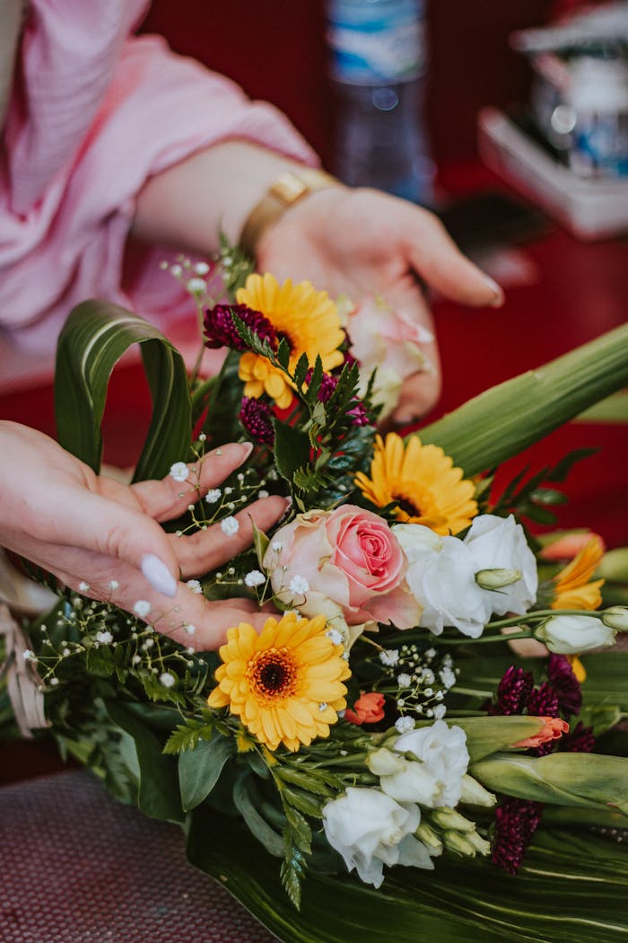 Colorful floral bouquet expertly arranged by a woman's hands, showcasing natural beauty and craft indoors.